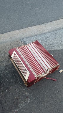 The remains of a red and white piano accordion. It is old and has recently had parts torn from it. It lies abandoned on a paved street sidewalk