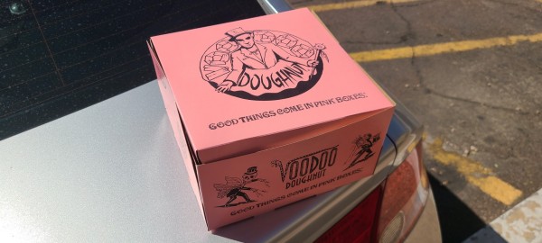 Pink box with a spooky dude popping out of a donut labeled "voodoo doughnut."
Underneath it reads "Good things come in pink boxes"