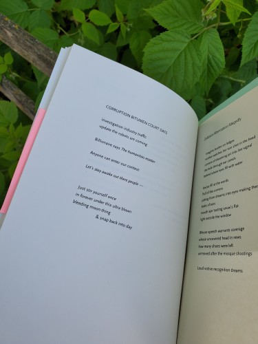 Poetry collection That Audible Slippage by Margaret Christakos (University of Alberta Press) is open to the poem "Corruption Bitumen Court Date". Bookmarks in pink and light green are visible sticking from pages of the book. The book is held up against a background of green leaves and thin, weathered wooden railings.

