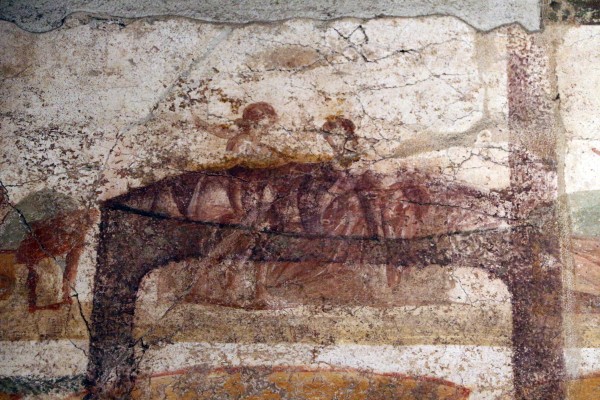 Two women, whose hair is the main indicator if the second figure's gender. The woman on the right is wearing a fascia pectoralis and lies back on a bed or a cline. The lesbian sex scene has been disfigured by patches of dark green colour, remains of the repainting of the wall that have been unable to be removed.