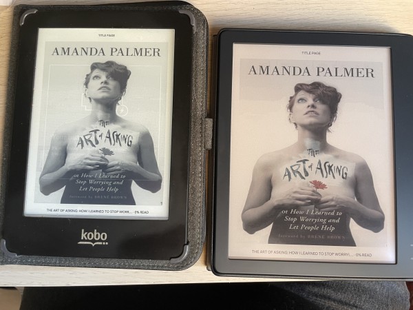 Een foto van een oude Kobo Glo en een nieuwe Kobo Libre Colour naast elkaar. Beiden hebben de titelpagina van Amanda Palmer's The Art Of Asking open. 